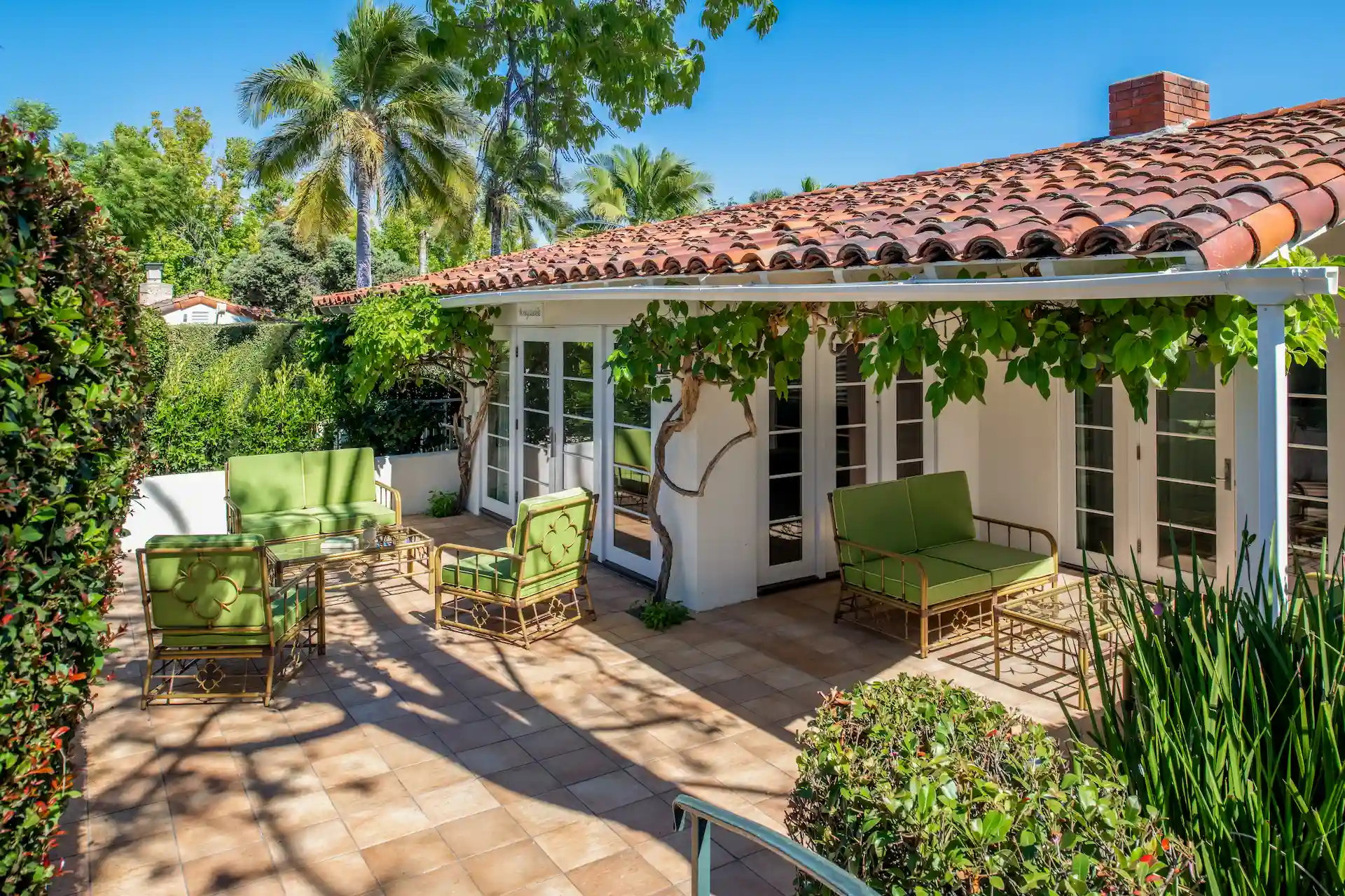 The Inn at Rancho Santa Fe: Bungalow patio with garden, a green sofa on the porch, on a sunny day with palm trees in the background.