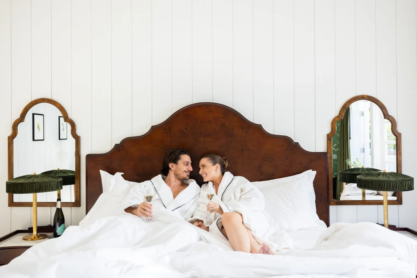 Newlyweds in bathrobes enjoying champagne in bed in their hotel room